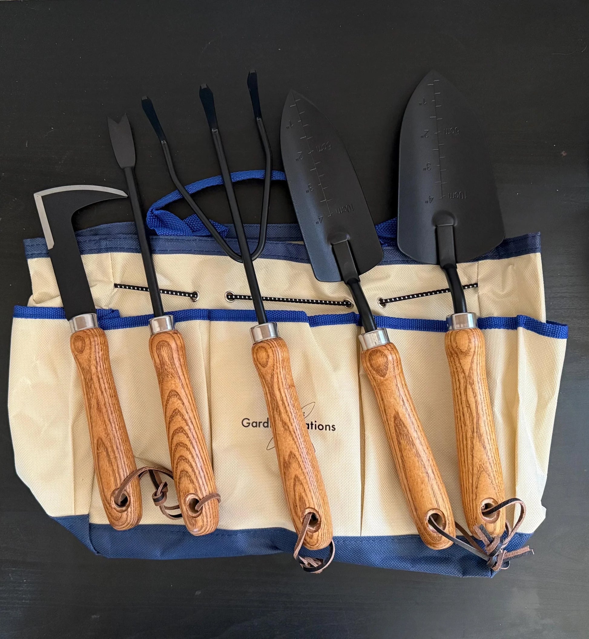 Five-piece gardening tool set with wooden handles and canvas storage tote on black background.