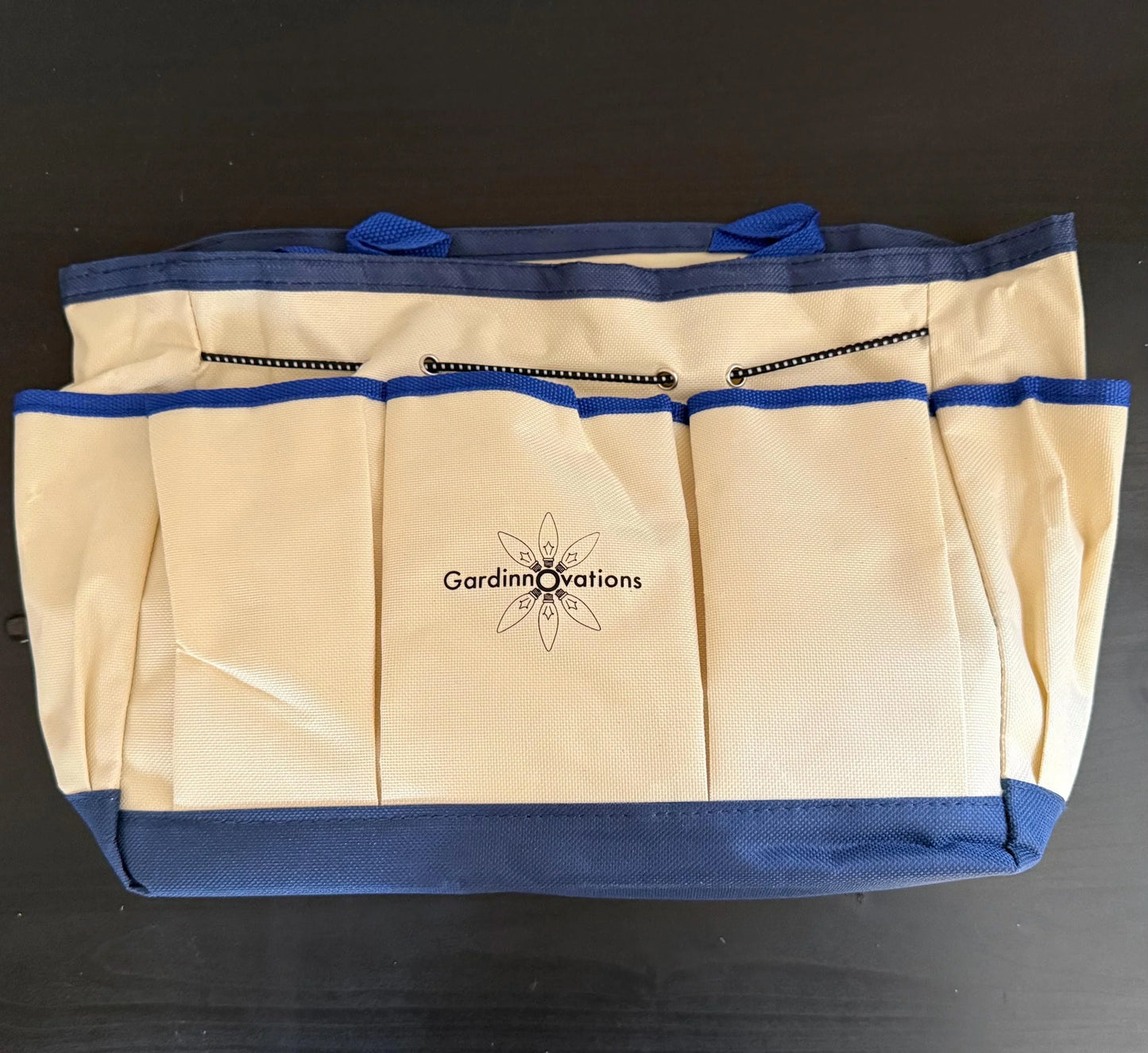 Beige and blue canvas garden tool bag with multiple pockets on a dark surface