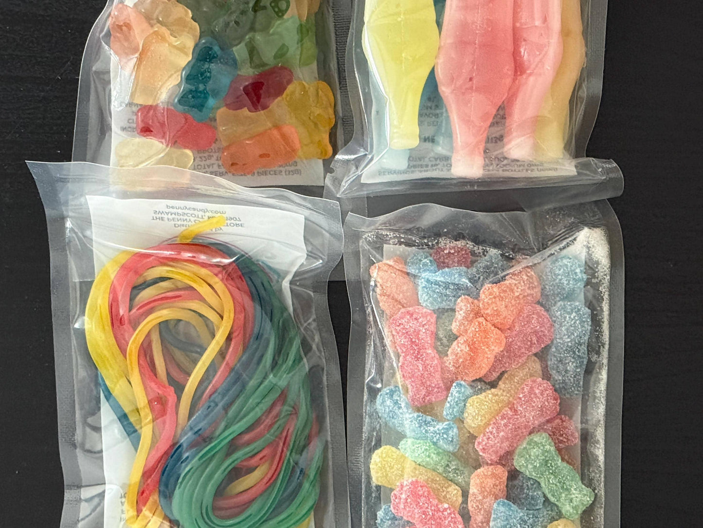 Assorted gummy candies in clear sealed bags, including gummy bears, sour gummies, cola bottles, and candy strings.