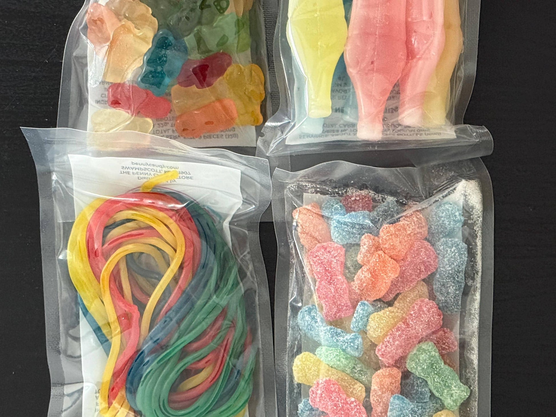 Assorted gummy candies in clear sealed bags, including gummy bears, sour gummies, cola bottles, and candy strings.