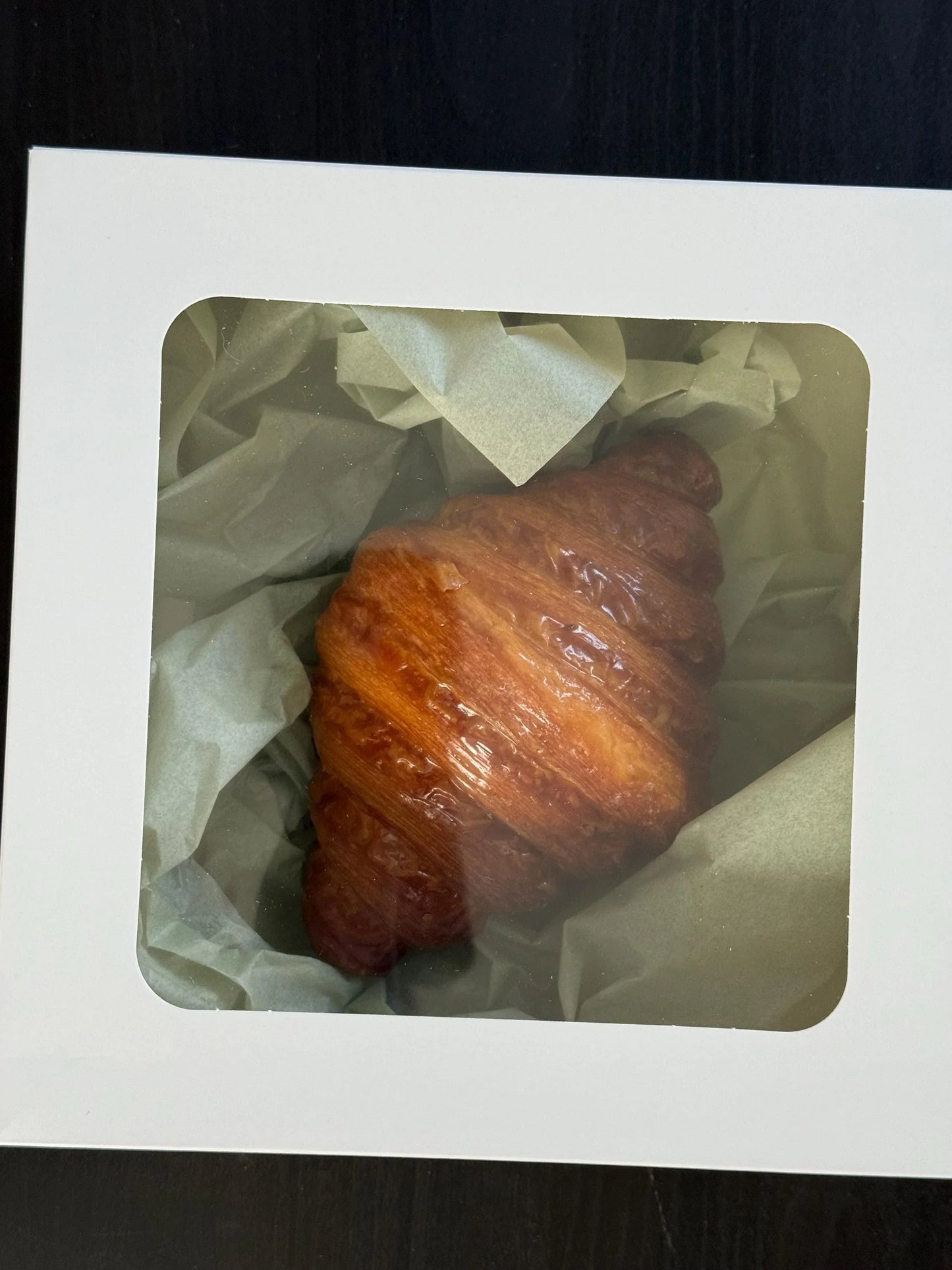 Fresh croissant in a white bakery box with tissue paper, perfect for gourmet gift giving