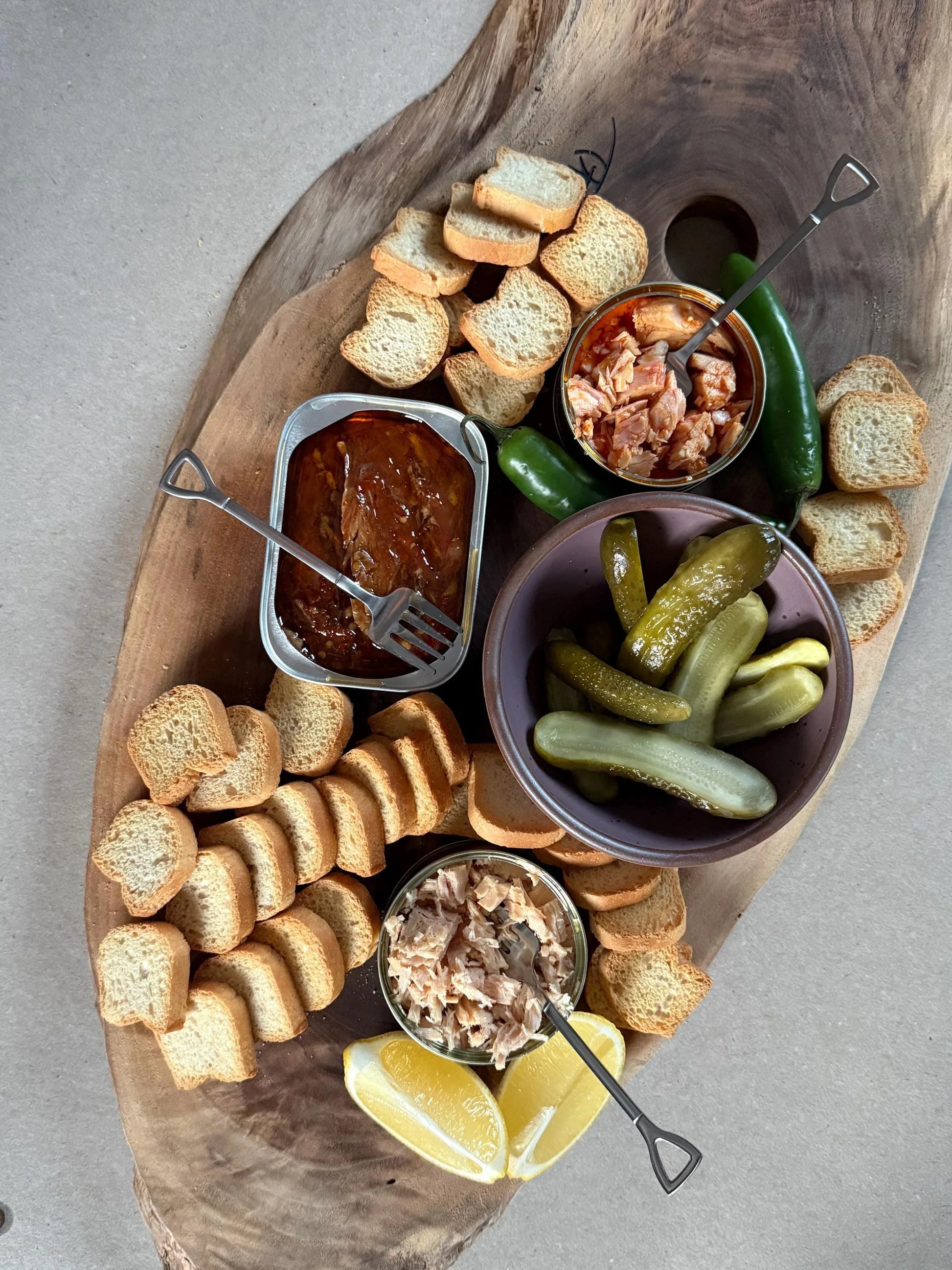 Charcuterie board with crostini, pickles, canned fish, lemon wedges, and jalapeños