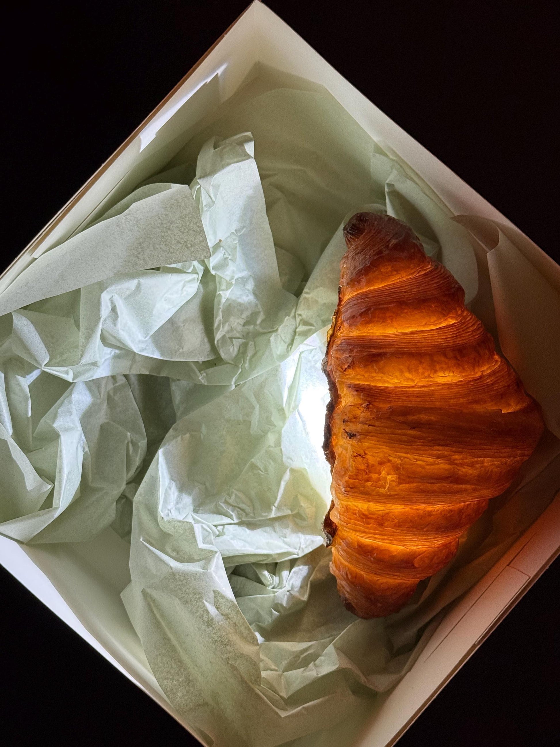 Realistic croissant shaped lamp glowing in a gift box with tissue paper