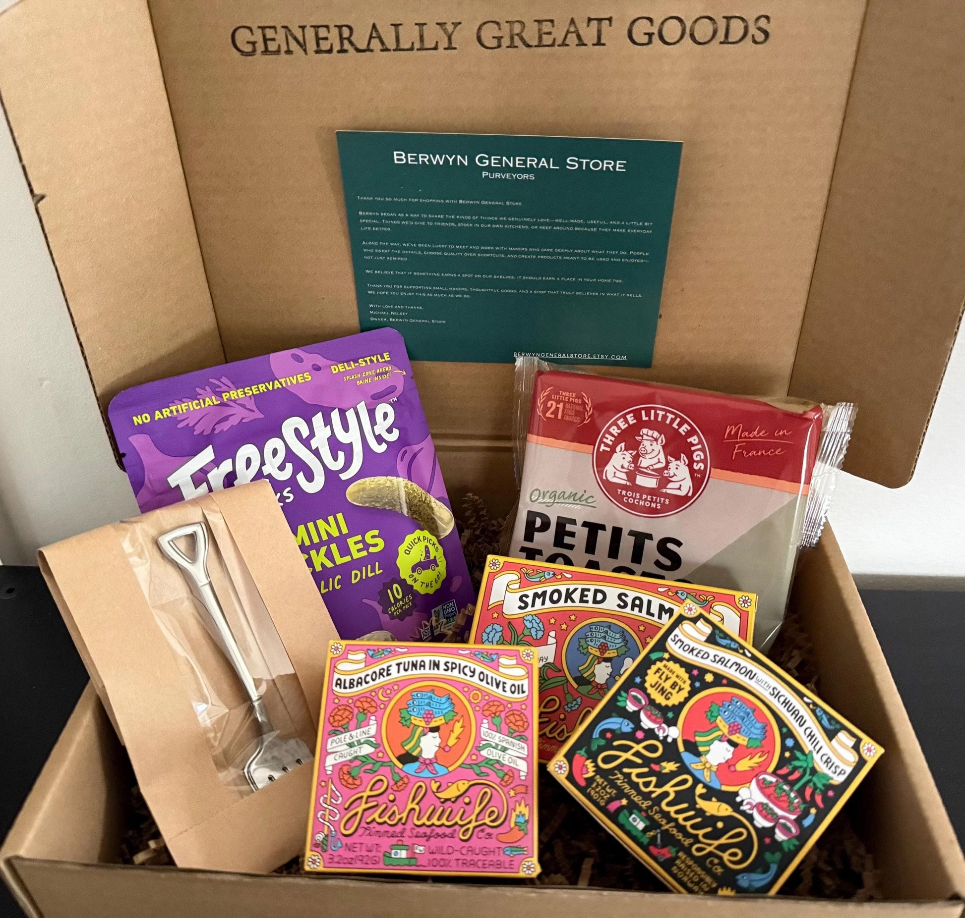 Gourmet gift box with pickles, crackers, canned fish, smoked salmon, and mini shovel.