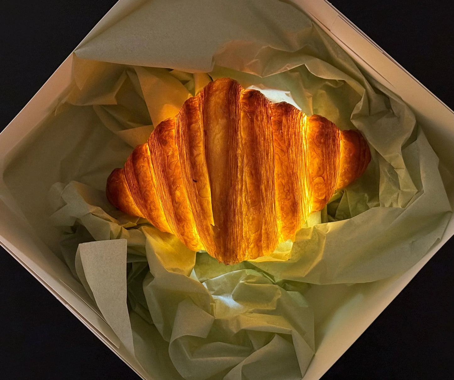 Realistic croissant-shaped lamp glowing in a gift box with tissue paper