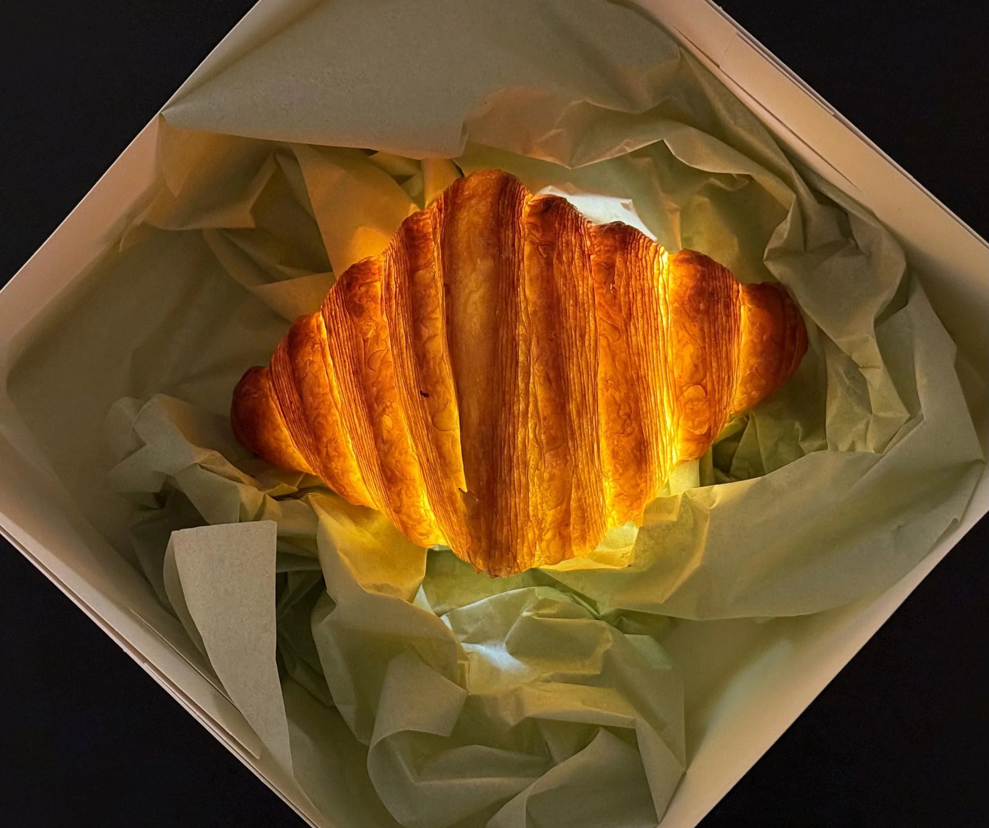 Realistic croissant-shaped lamp glowing in a gift box with tissue paper
