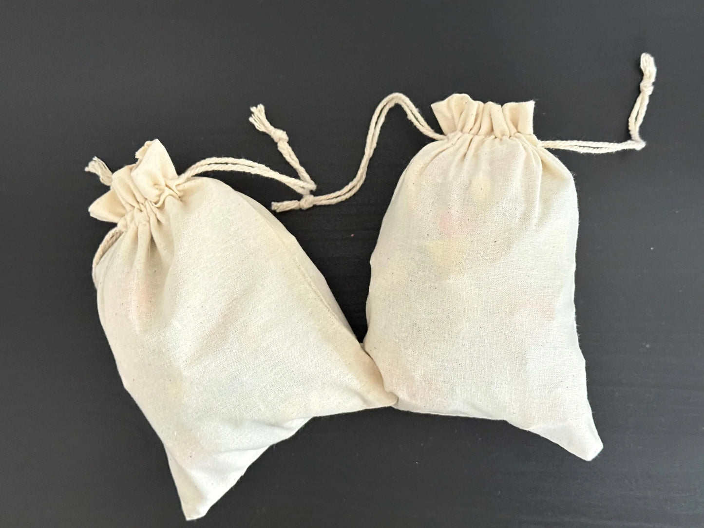 Two small cotton drawstring gift bags on a dark background, ideal for artisan goods or favors.
