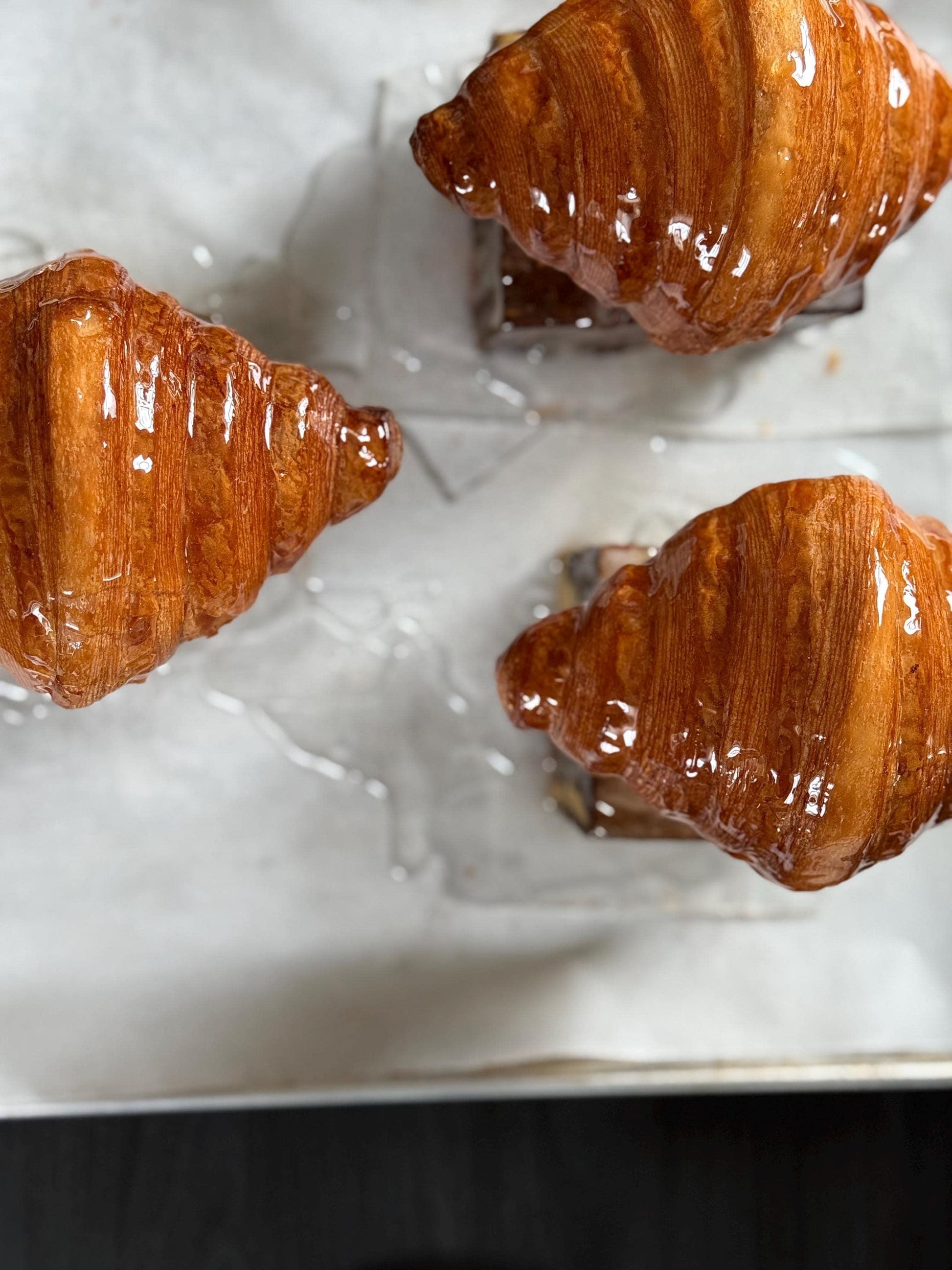 Glazed croissants with a golden, flaky crust on parchment paper, gourmet pastry closeup