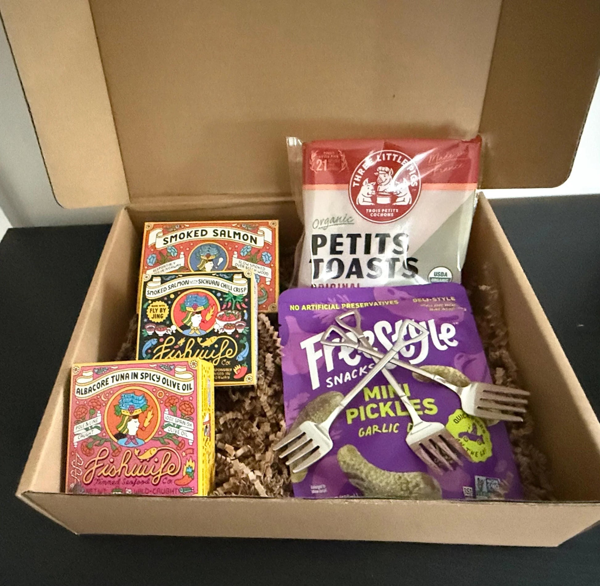 Gift box with smoked salmon, albacore tuna, toasts, garlic pickles, and mini forks.