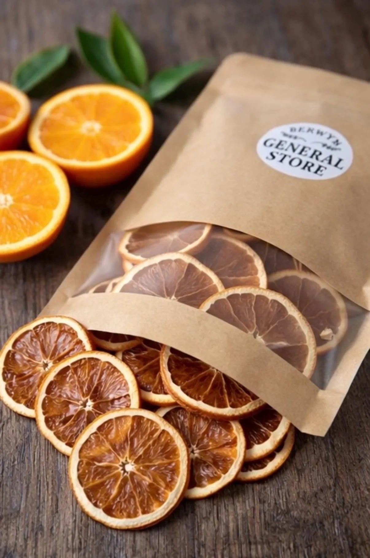 Dried orange slices in resealable kraft bag on rustic wood with fresh oranges and leaves