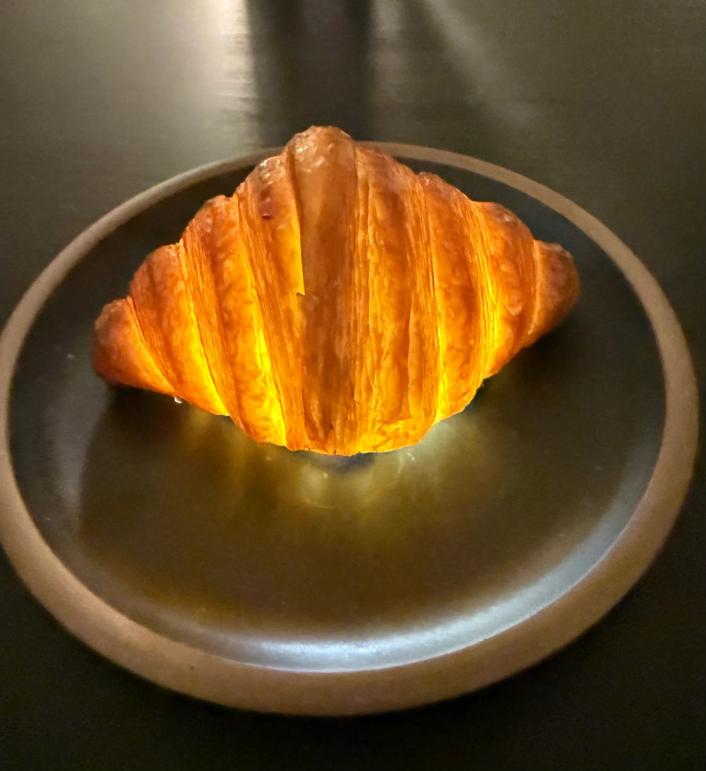 Golden croissant-shaped lamp glowing on a dark plate, artisan home decor