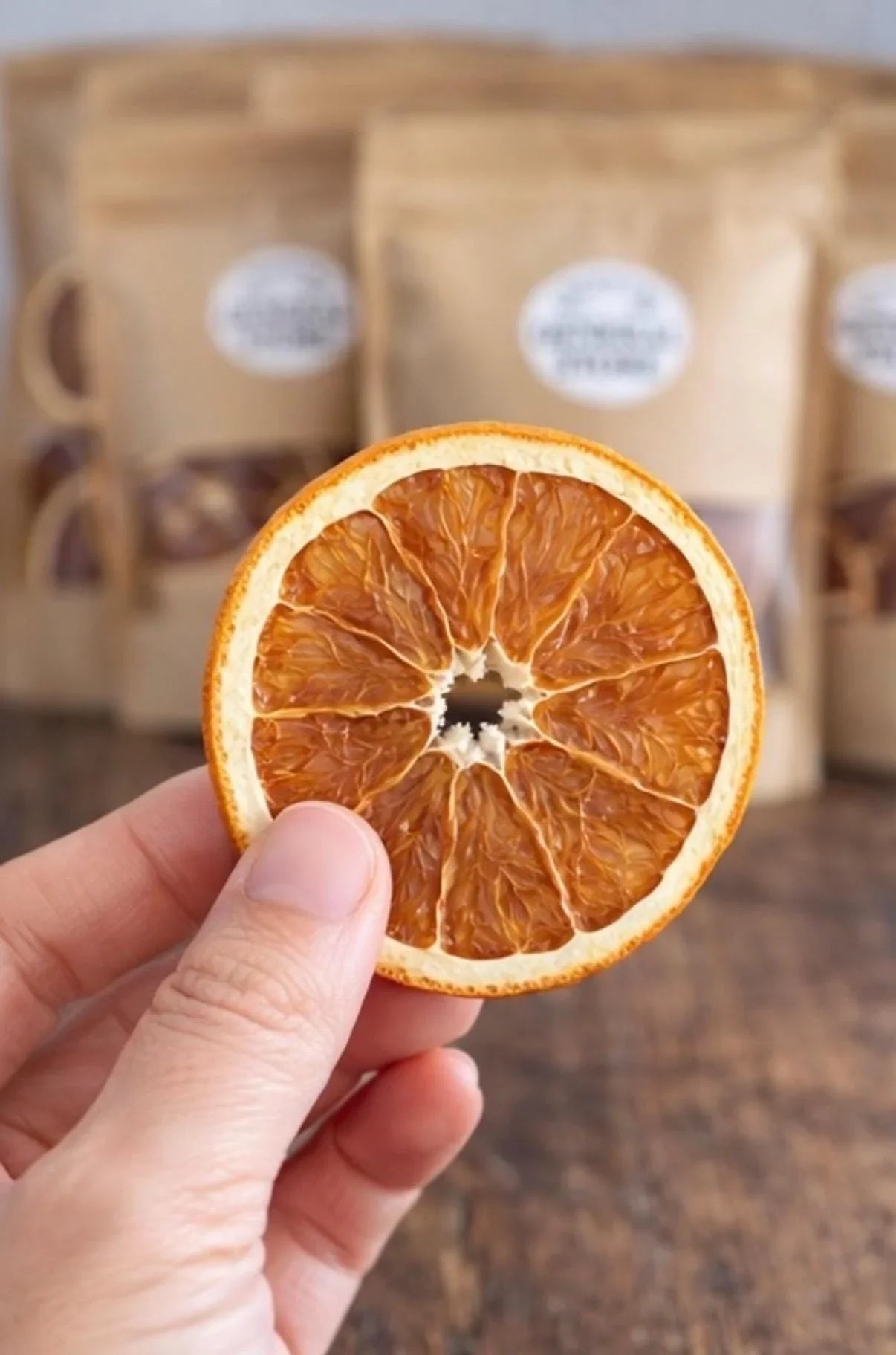 Hand holding a dried orange slice with brown kraft packaging in the background.