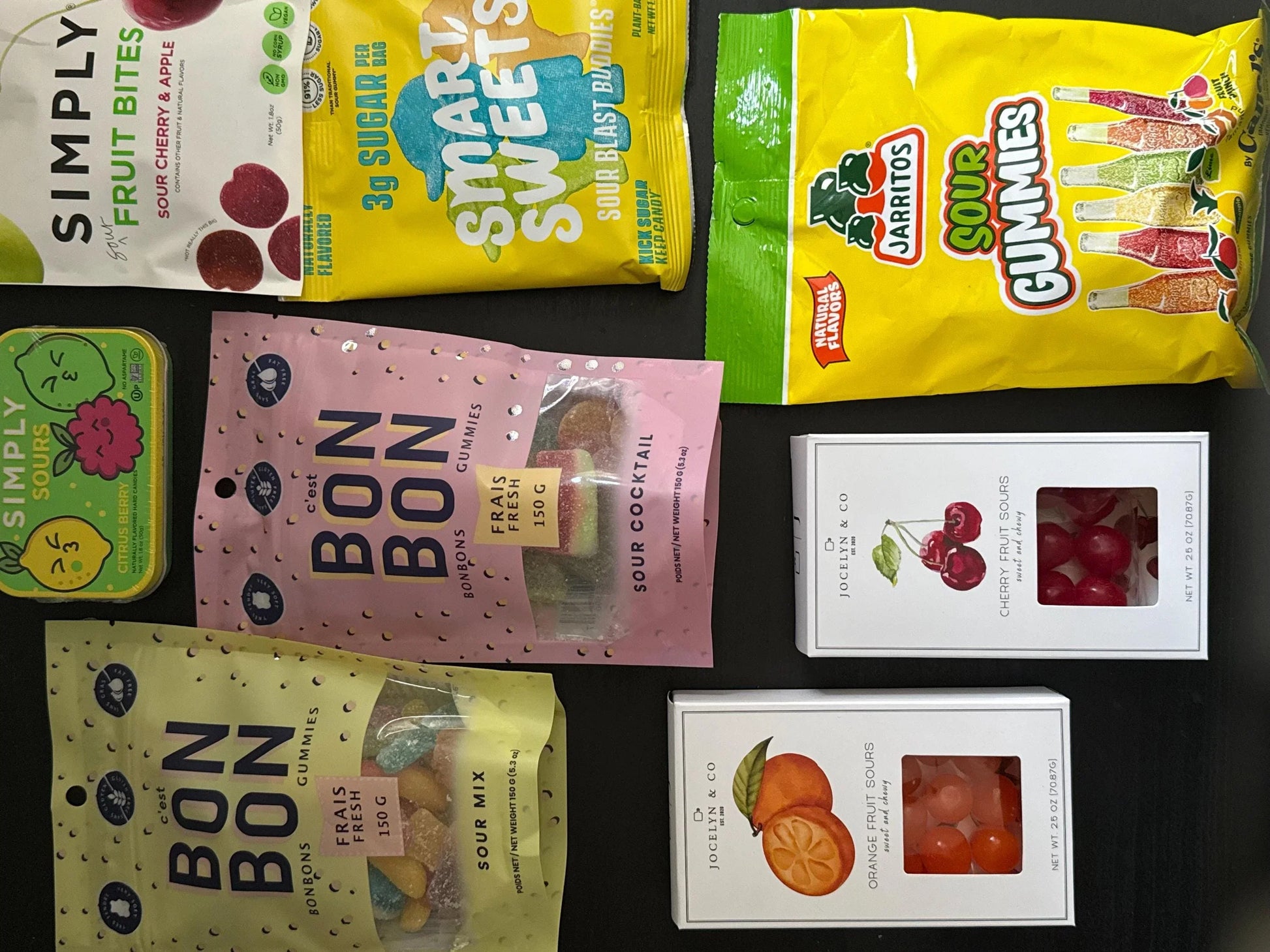Assorted sour candy gift set with gummies, fruit bites, and colorful packaging on black background