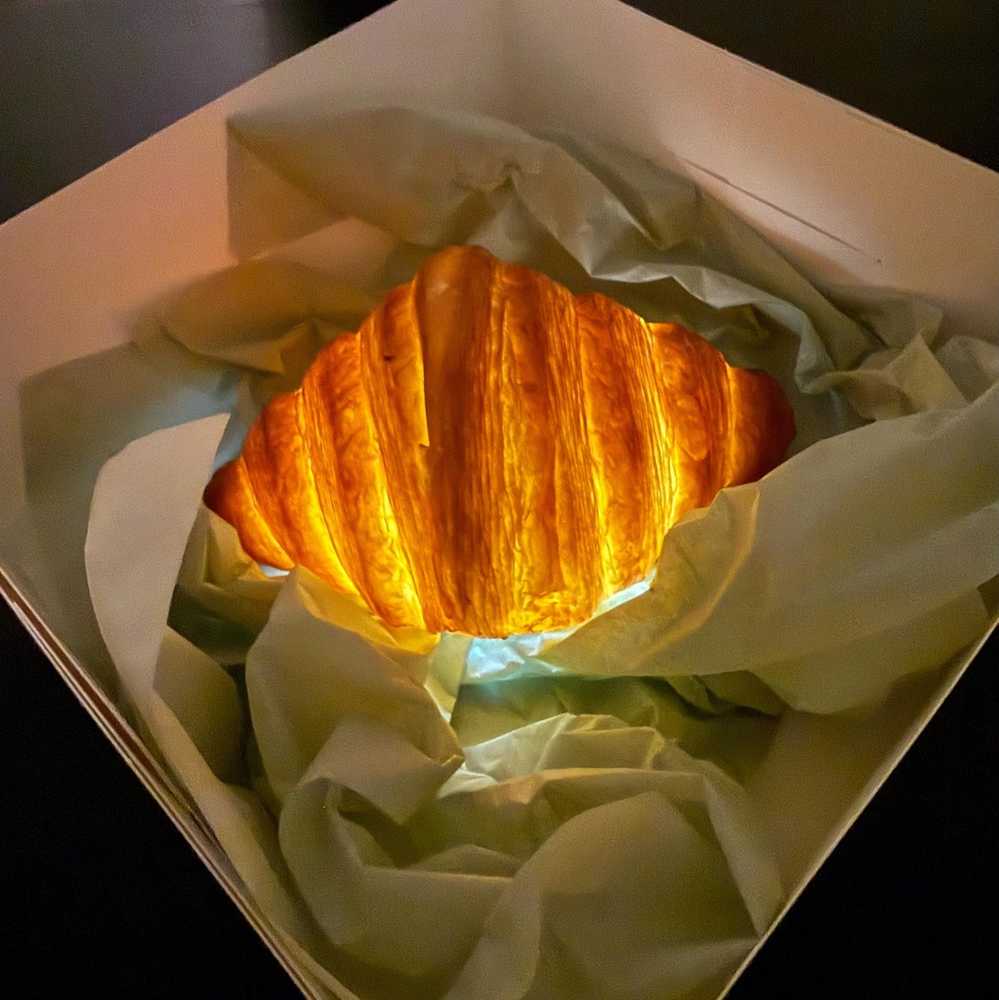 Realistic croissant-shaped night light glowing in a gift box with tissue paper