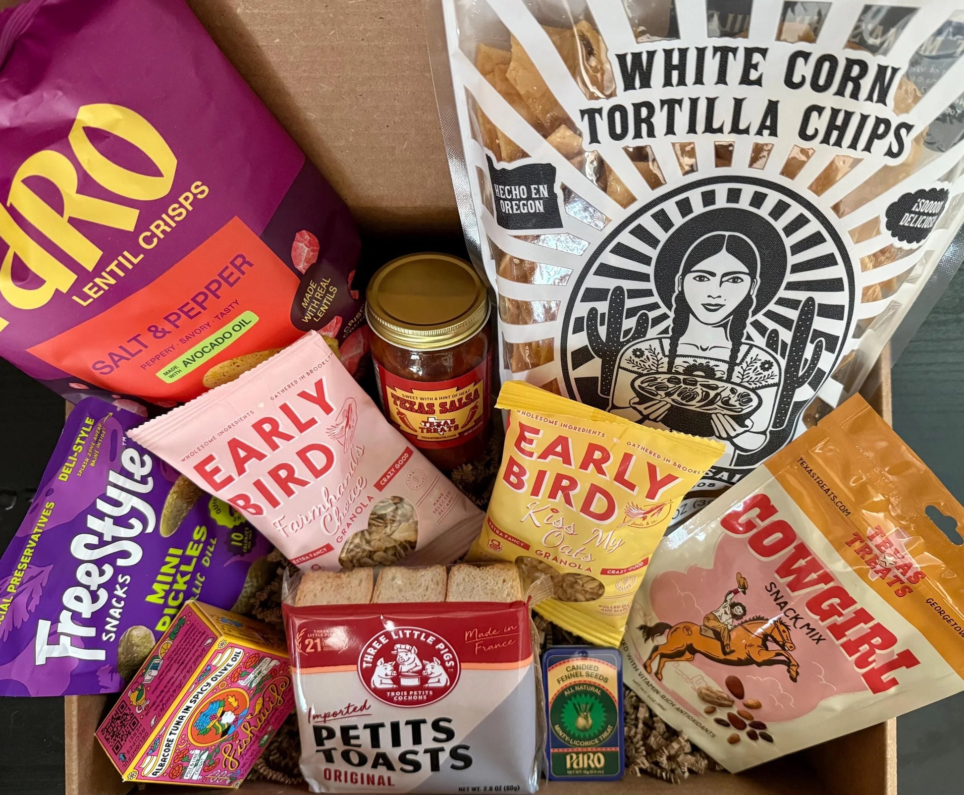 Assorted gourmet snacks and treats gift box with chips, granola, and preserves.