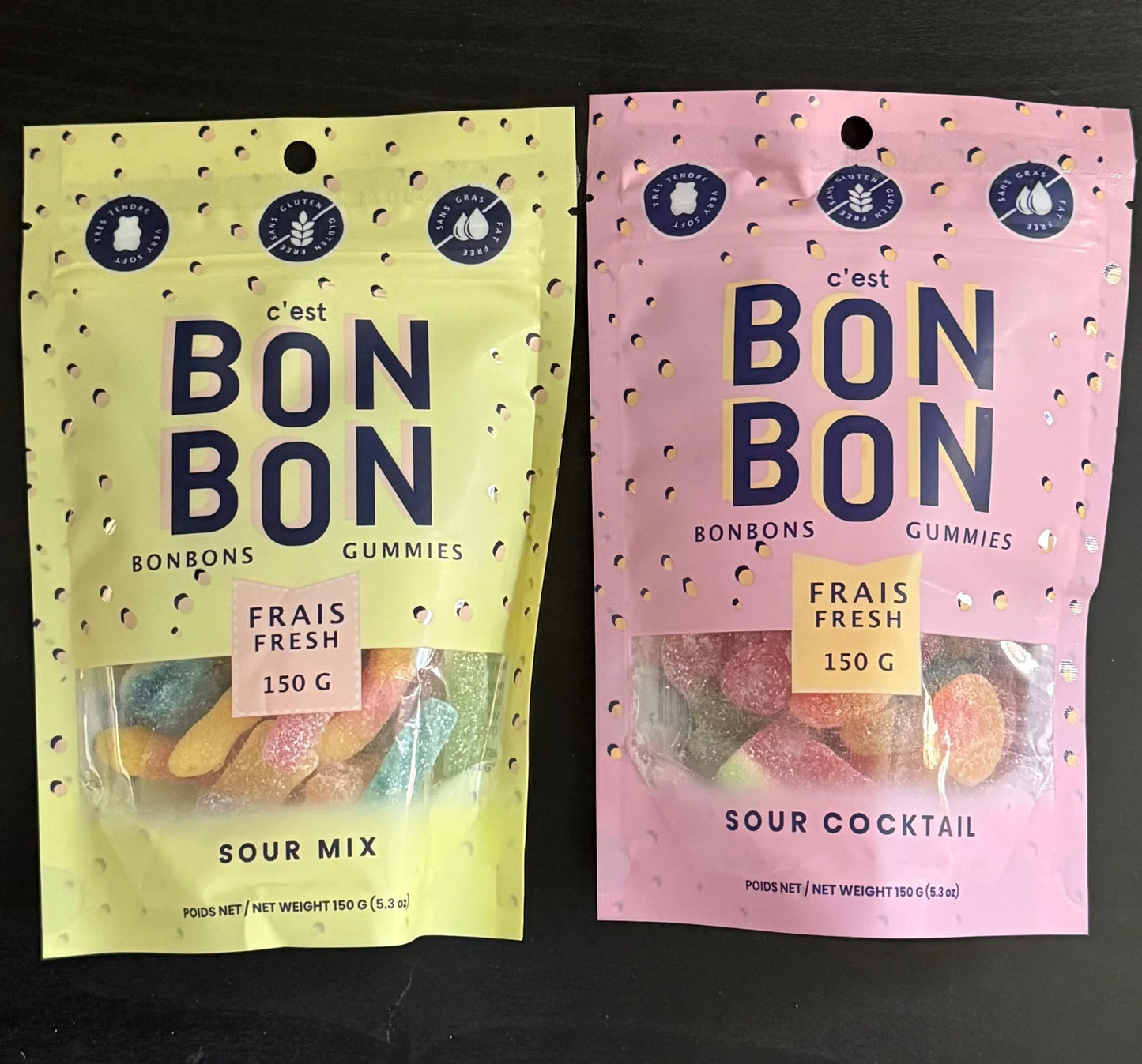 Two colorful C'est Bonbon gummy candy pouches, Sour Mix and Sour Cocktail, on dark background.